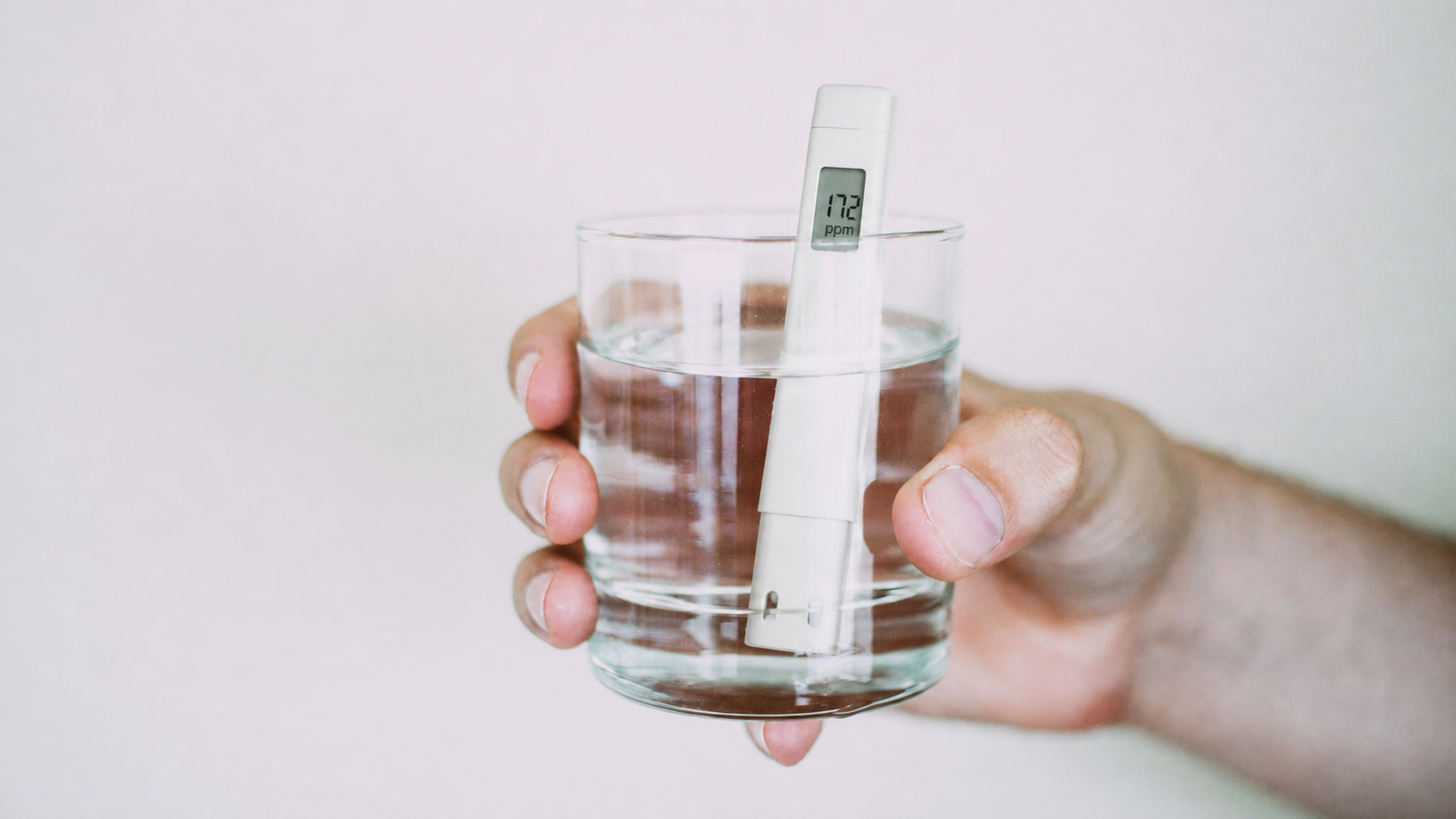 Testeur TDS plongé dans un verre d’eau tenu à la main